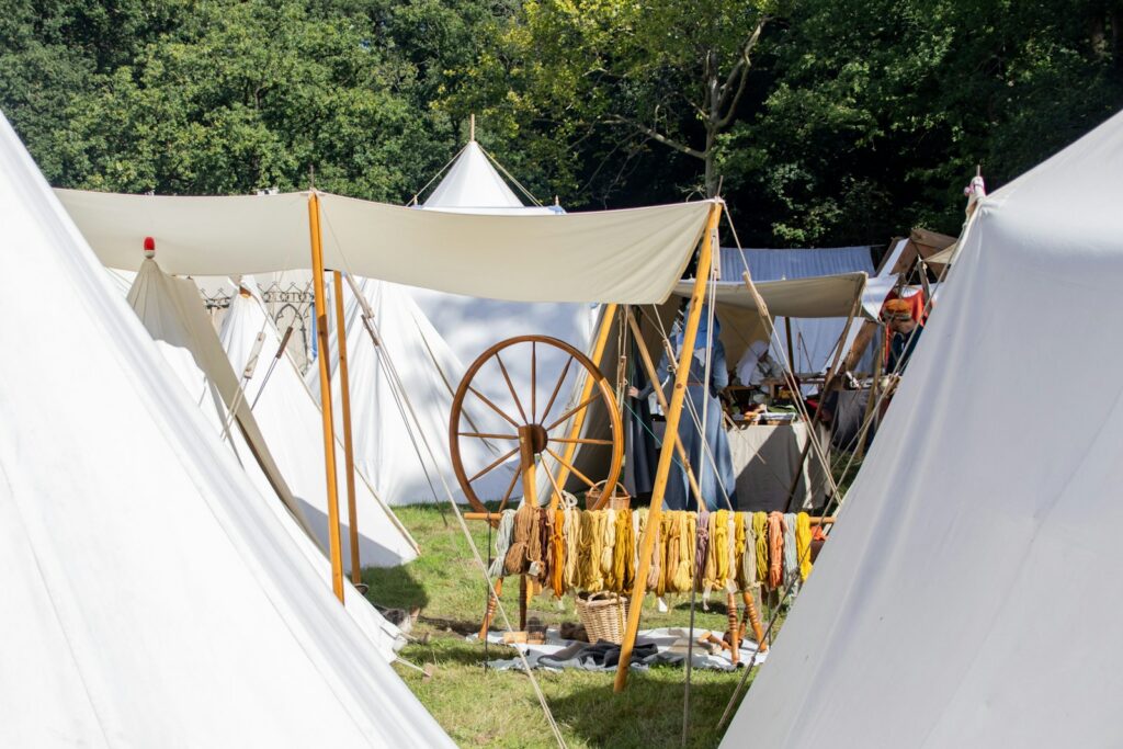 Campement de reconstitution médiévale avec tentes blanches, rouet et écheveaux de laine teinte